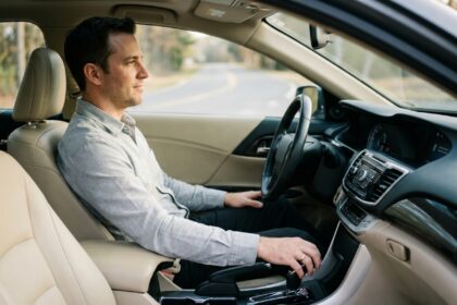 Homme au volant d'une voiture avec boîte automatique, main posée sur le levier de vitesse, intérieur moderne en cuir beige